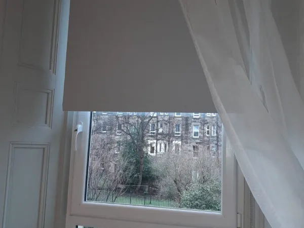 Grey roller blind with voile in a tenement bay window