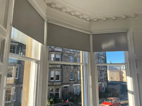 Grey roller blinds on an Edinburgh bay window with traditional tenement views